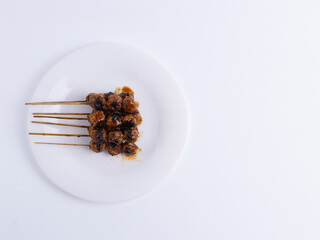 An top view of Indonesian grilled meatball satay with spicy peanut sauce on a white plate with copy space. Concepts for Asian street food, traditional, grilled, snack, savory, spicy, isolated.
