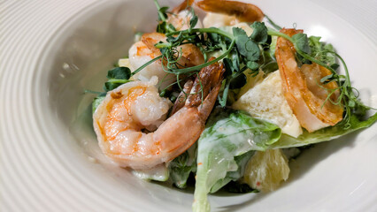 Close-up of salad with shrimps, orange, avocado, mixed greens under hot-sweet lime sauce in white plate