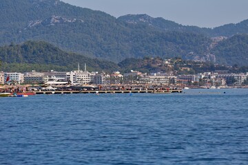 Fototapeta premium Seascape with a coastal city and mountains in the background, under a sunny sky. The water is deep blue, and several buildings are visible in Marmaris - Mugla - Turkey