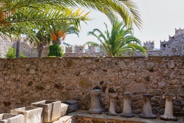 A stone wall and turret with palm trees behind it, taken at eye level. There are stone basins and carved columns in the foreground in Marmaris Castle - Marmaris - Mugla - Turkey © Robert