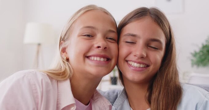 Close up of two cheerful sisters or friends giving each other high five and celebrating their success. Smiling preteen girls, sitting on couch at home, looking at camera, touching heads to each other.