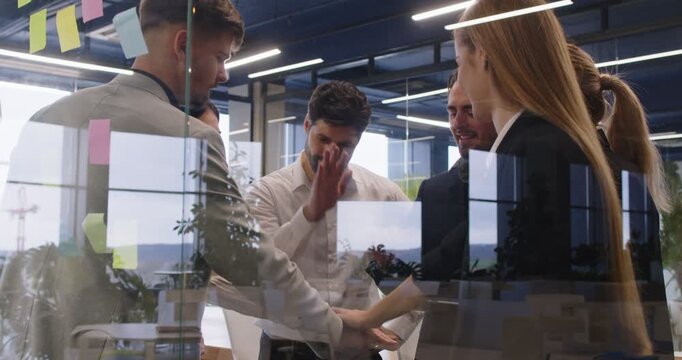 Motivated team happy getting joining to raise high fives finding problem solution, successful brainstorm result, workers unity celebrate good common achievement behind modern glass office wall