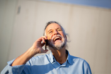 Happy older man laughing during phone call in sunlight