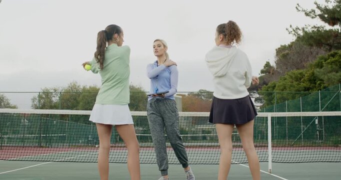 Coach approaching female players holding balls, teaching backhand swing with tablet on court