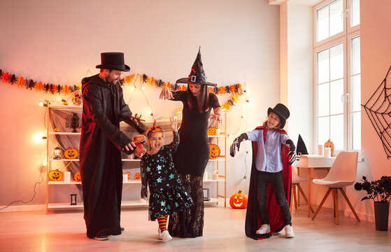 Happy family having fun on Halloween. Parents and children dress up in spooky costumes and play together. Mom, dad and kids disguised as witches, wizard and skeleton rehearsing dance for festive event - Powered by Adobe