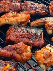 A close-up shot of marinated pork ribs and chicken pieces cooking on a hot barbecue grill with smoky char marks.

