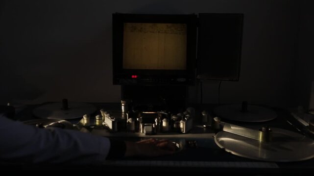 This close-up video captures the intricate details of a vintage film editing machine in action. The machine features spools of film, intricate mechanical parts, and a well-lit workspace