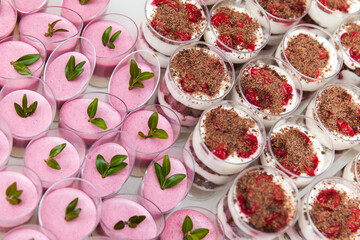 Assortment of mini desserts in glass cups with mousse, layered cream, chocolate, and berries on a festive buffet table.