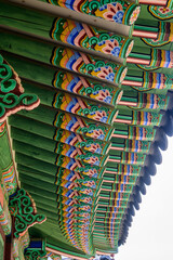 Naklejka premium Detailed, colorful eaves of a traditional Korean building at Deoksugung Palace in Seoul, South Korea. Dancheong painting adds ornamentation and protection to wooden surfaces.