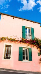 Pink house with green shutters, flowers, and blue sky