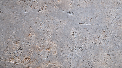Grey and brown stone wall with many holes. The wall is rough and uneven. The holes are scattered all over the wall, some are small and others are large. The wall appears to be old and worn down