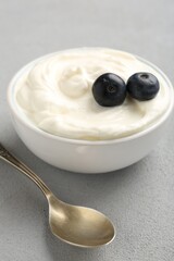Delicious yogurt in bowl, blueberries and spoon on grey table, closeup