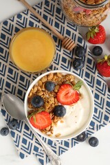 Tasty yogurt with granola, berries and honey on white table, flat lay