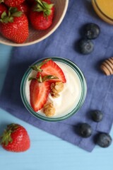 Tasty yogurt with granola and berries on light blue wooden table, flat lay