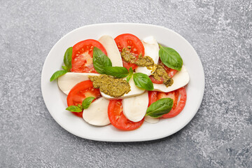 Tasty salad Caprese with mozzarella, tomatoes, basil and pesto sauce on grey table, top view
