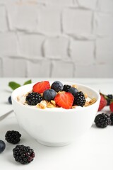 Tasty yogurt with granola and berries in bowl on white table, closeup. Space for text