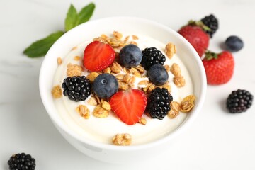 Tasty yogurt with granola and berries in bowl on white marble table, closeup