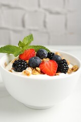 Tasty yogurt with granola and berries in bowl on white table, closeup