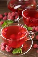 Tasty raspberry tea in glass cups, teapot, berries and mint on wooden table, closeup