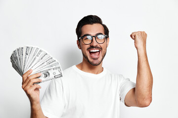 Happy cheerful man in glasses celebrating success, holding fan of money while standing against plain white background. Financial success concept.