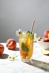 Tasty iced peach tea in glass, fresh fruits, mint and chamomile flowers on white table
