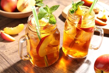 Refreshing iced peach tea with mint in mason jars and fresh fruits on wooden table, closeup