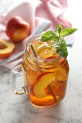 Refreshing iced peach tea with mint in mason jar on white marble table, closeup