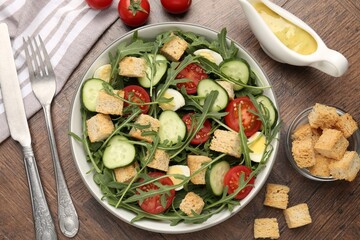 Tasty salad with croutons, cucumbers, tomatoes and arugula on wooden table, flat lay