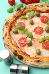 Delicious pizza with tomatoes, basil and olives on turquoise background, closeup