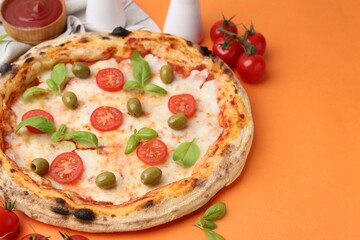 Delicious pizza with tomatoes, basil and olives served on orange background, closeup. Space for text