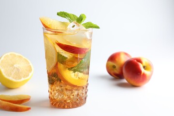Tasty iced tea with lemon, peaches and mint on white background