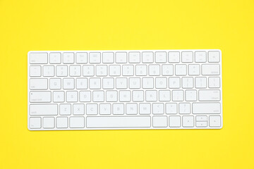 Modern white wireless keyboard on yellow background, top view