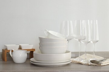 Different clean white dishware, glasses and cutlery on counter in kitchen