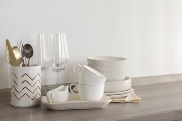 Different clean white dishware, glasses and cutlery on counter in kitchen