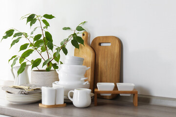 Different clean white dishware, wooden cutting boards, cutlery and houseplant on counter in kitchen