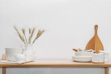 Different clean white dishware, cutting board and spikes on wooden table indoors