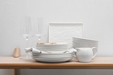 Different clean white dishware and glasses on wooden table indoors