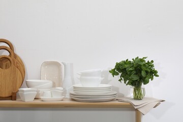 Clean dishware, cutting boards and mint on wooden table near white wall