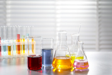 Laboratory glassware with different samples and test tubes on light table indoors. Solution chemistry