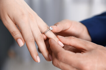Making proposal. Man putting engagement ring on his girlfriend's finger indoors, closeup