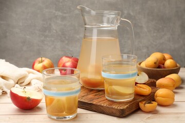 Tasty compot in glasses, jug, fresh apricots and apples on wooden table