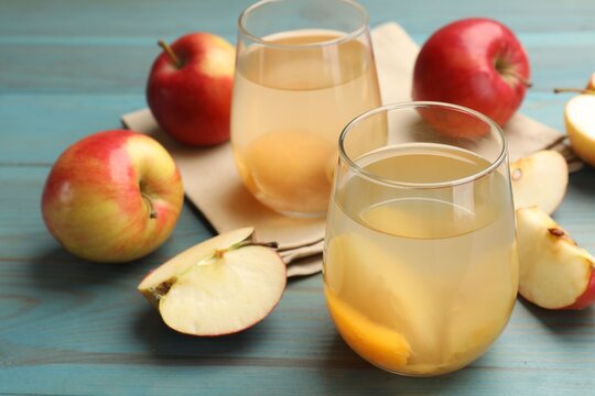 Tasty compot in glasses and fresh apples on light blue wooden table, closeup