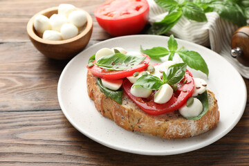 Delicious sandwich with mozzarella cheese, tomatoes and basil on wooden table, closeup