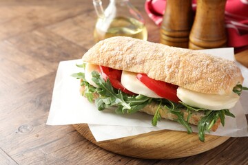 Delicious sandwich with mozzarella cheese, tomato and arugula on wooden table, closeup. Space for text