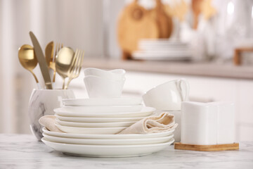 Different clean white dishware, cups and cutlery on marble table indoors