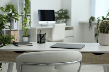 Stylish workplace with laptop, stationery and floral decor in office. Biophilic interior design