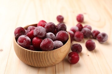 Ripe frozen cherries and bowl on light wooden table, closeup