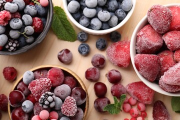 Different ripe frozen berries and mint leaves on light wooden table, flat lay
