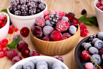 Different ripe frozen berries and mint leaves on light wooden table, closeup