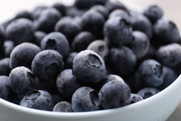 Ripe frozen blueberries in bowl on grey table, closeup